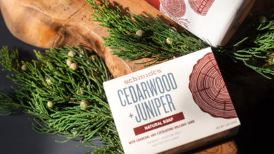 Schmidt's Cedarwood+Juniper Bar Soap on a wood block and surrounded by tree leaves